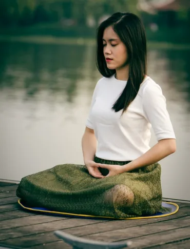 woman meditating on wooden dock during daytime
