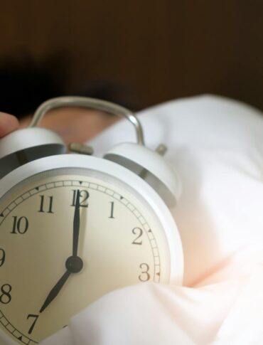 A close-up of a hand reaching for a ringing alarm clock, symbolizing waking up in the morning.