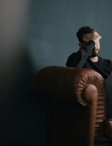 a man holds his head while sitting on a sofa